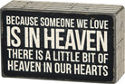 Decorative sign with text 'Because someone we love is in heaven, there is a little bit of heaven in our hearts' on a black background.