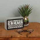Decorative sign with a quote, glasses, and a plant on a wooden surface.