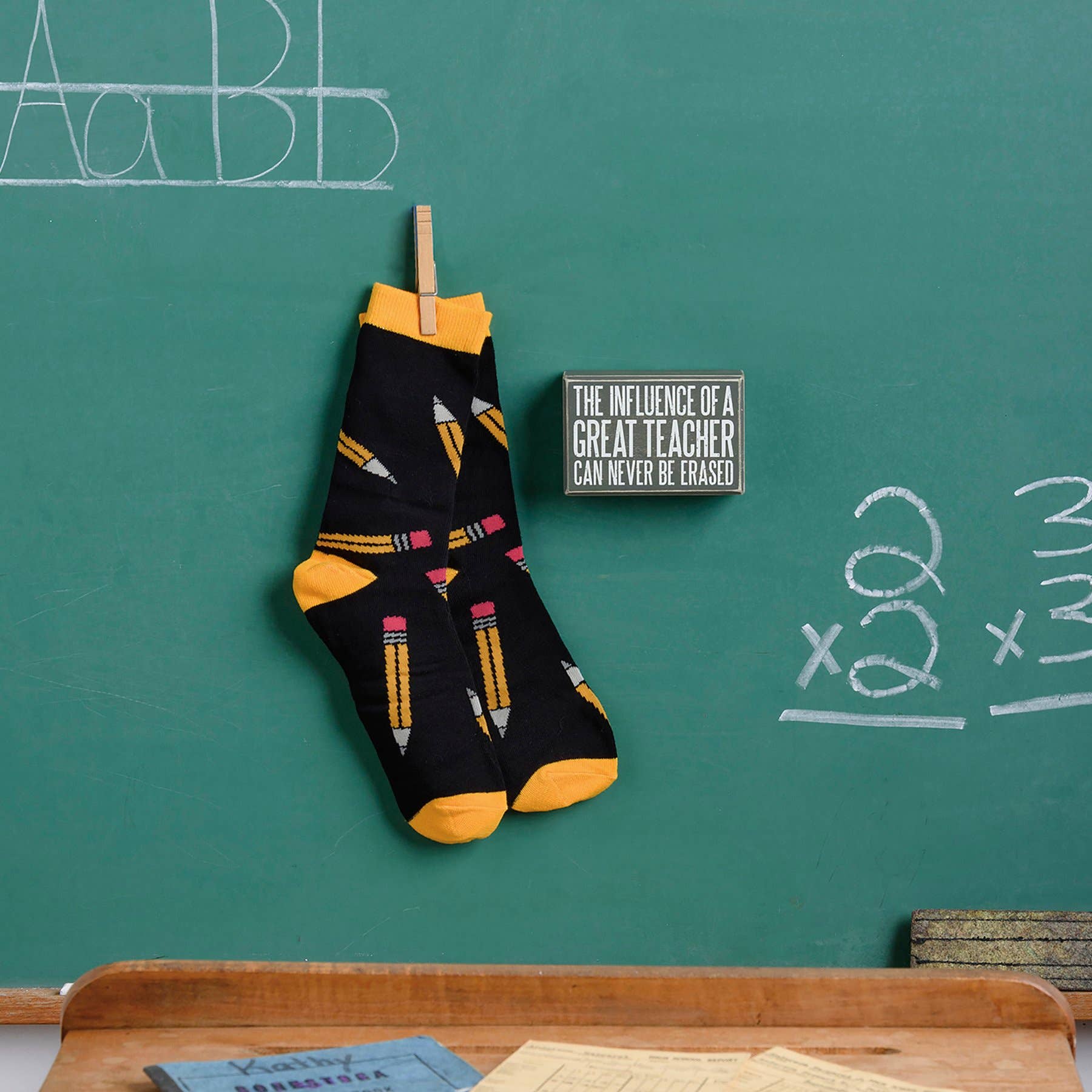 Black socks with yellow accents hanging on a chalkboard with educational drawings.
