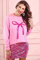 a light pink long-sleeve pullover made from luxe material with drop shoulder, a crew neckline, and a foil bow outlined in delicate pearls