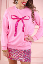 a light pink long-sleeve pullover made from luxe material with drop shoulder, a crew neckline, and a foil bow outlined in delicate pearls