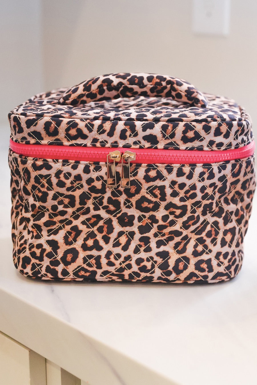 a structured bag with a spacious interior, a secure double zip around closure, a top handle, and gold accents on a quilted body in safari chic (leopard)