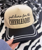 a lightweight unisex embroidered hat with black script 'just here for the' lettering, bold block 'CHEERLEADERS' text, contrasting black bill, white piped trim, cream structured front, black top button, and adjustable snap-back closure