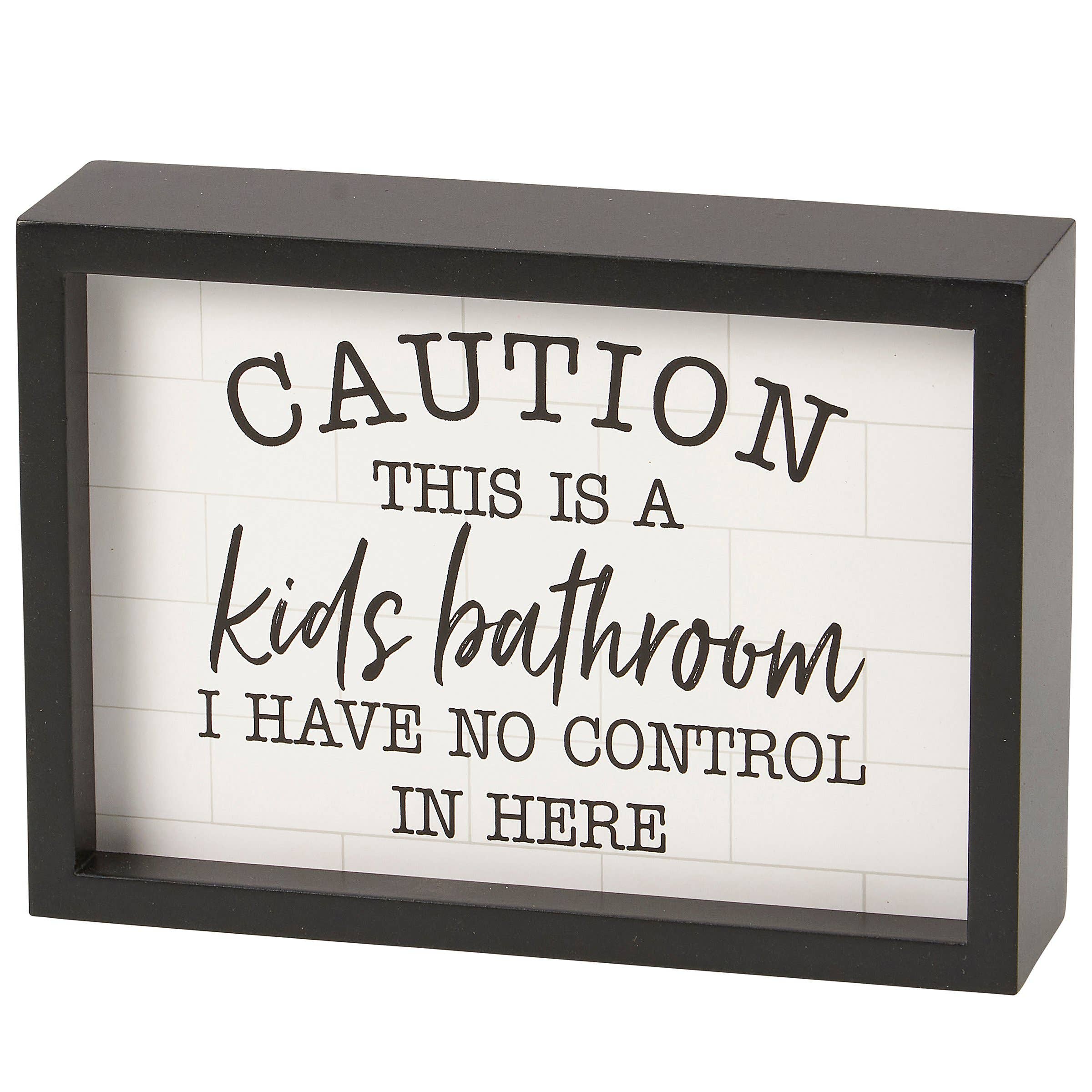 Decorative sign with text 'Caution: This is a kids' bathroom. I have no control in here.' in a black frame.