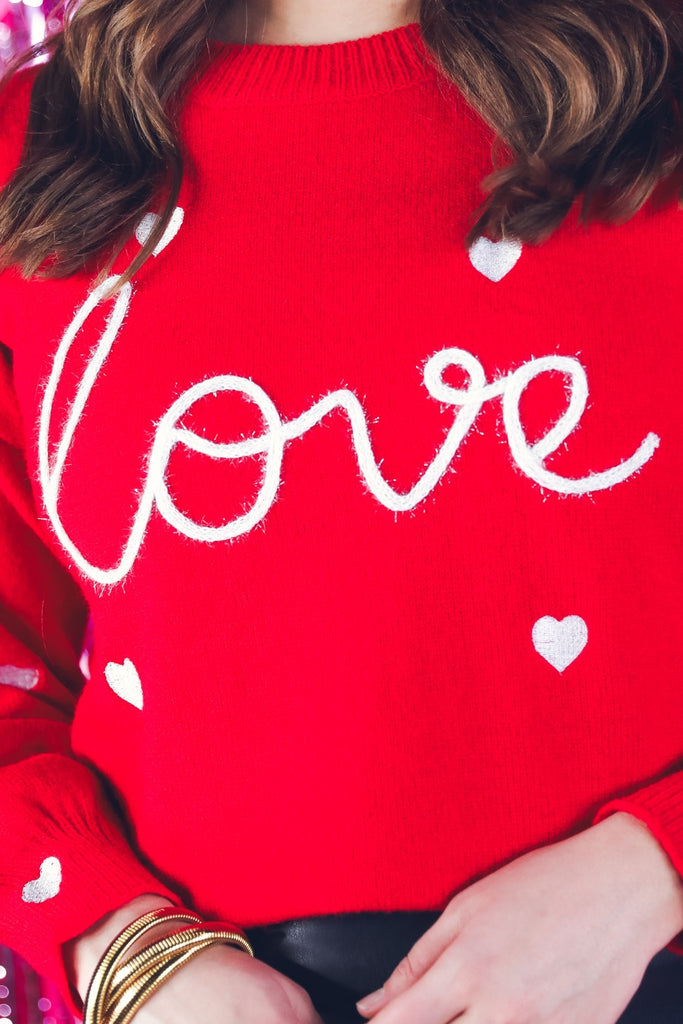 red long sleeve sweater with white embroidered hearts & "love" spelled out in tinsel-style writing