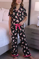 Young girl wearing a black pajama set with pink accents in a bedroom.