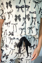 short sleeve top and matching pants on white base with a black bow pattern, black piping, and black ruffle trim