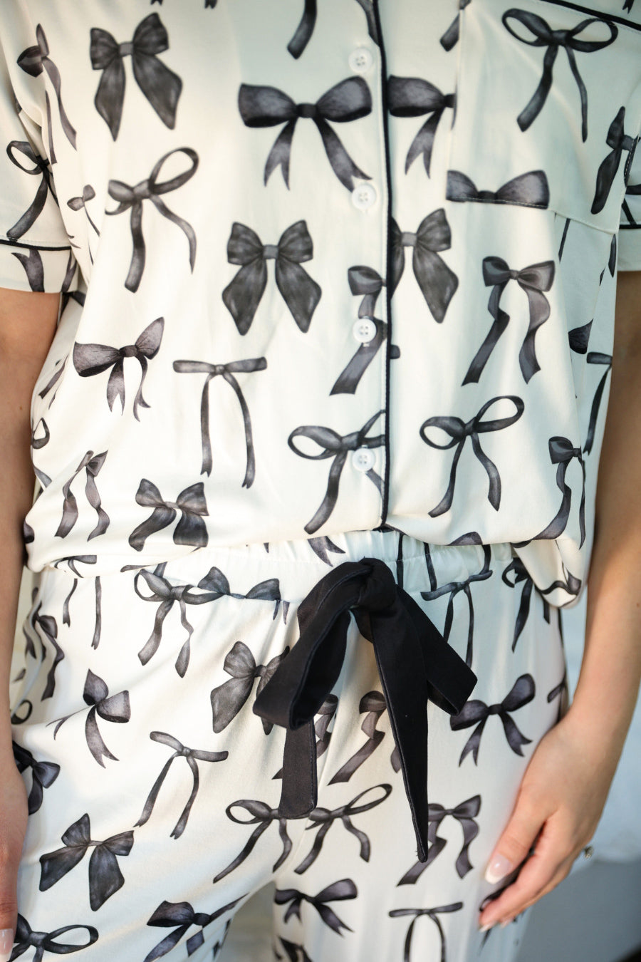 short sleeve top and matching pants on white base with a black bow pattern, black piping, and black ruffle trim