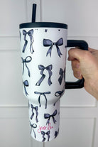 40-ounce white tumbler with a black bow and ribbon pattern print design, handle, screw-on lid, and a reusable straw
