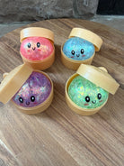 a mystery bead-filled mini dumpling squishy with assorted colors, iridescent shimmer, kawaii face, steamer-style container, and soft sensory texture in blue, green, pink, and purple