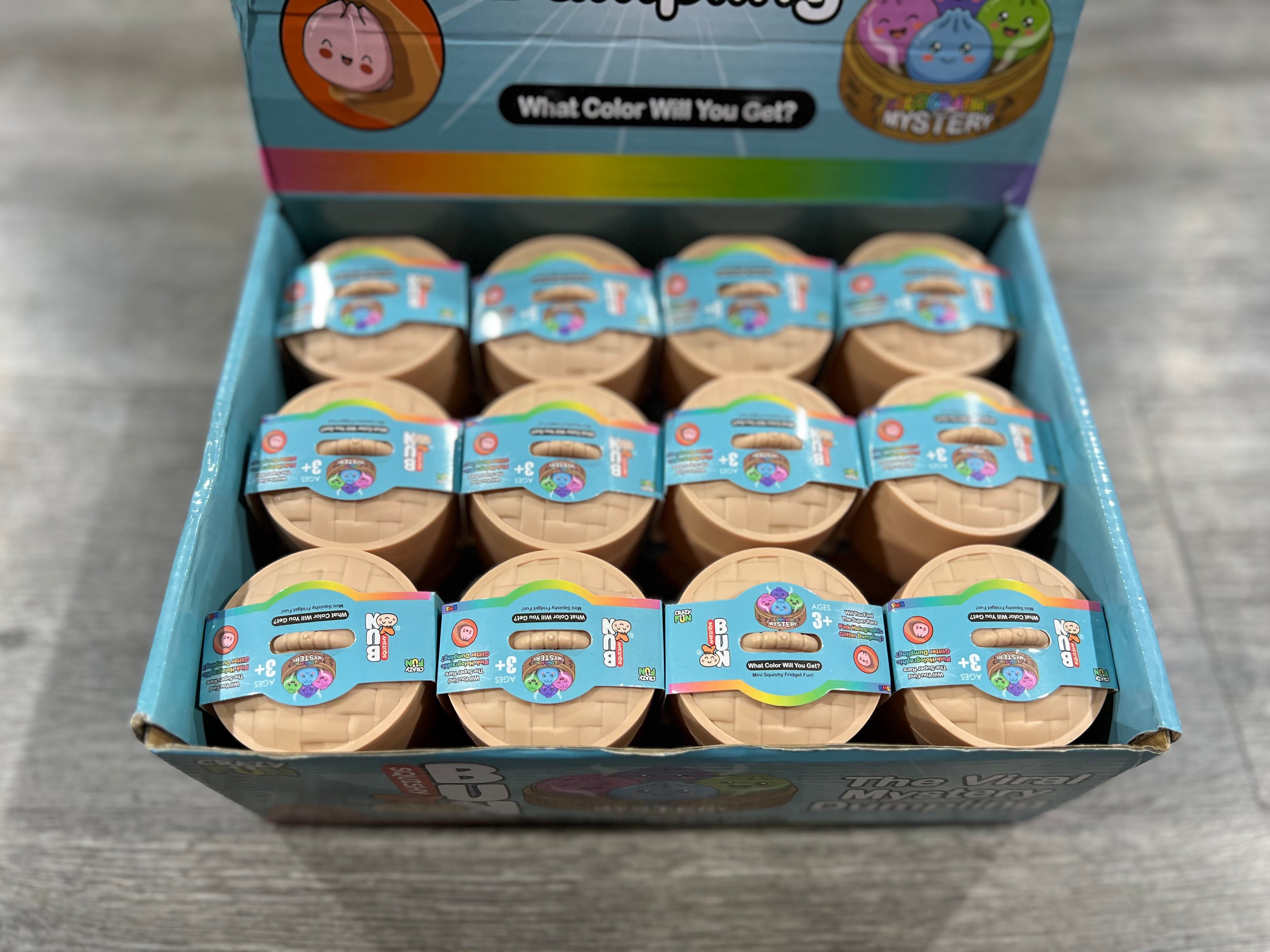 A retail display box filled with multiple small round mystery toy containers. The box is light blue with colorful graphics and text including 'What Color Will You Get?' and 'Mystery'.