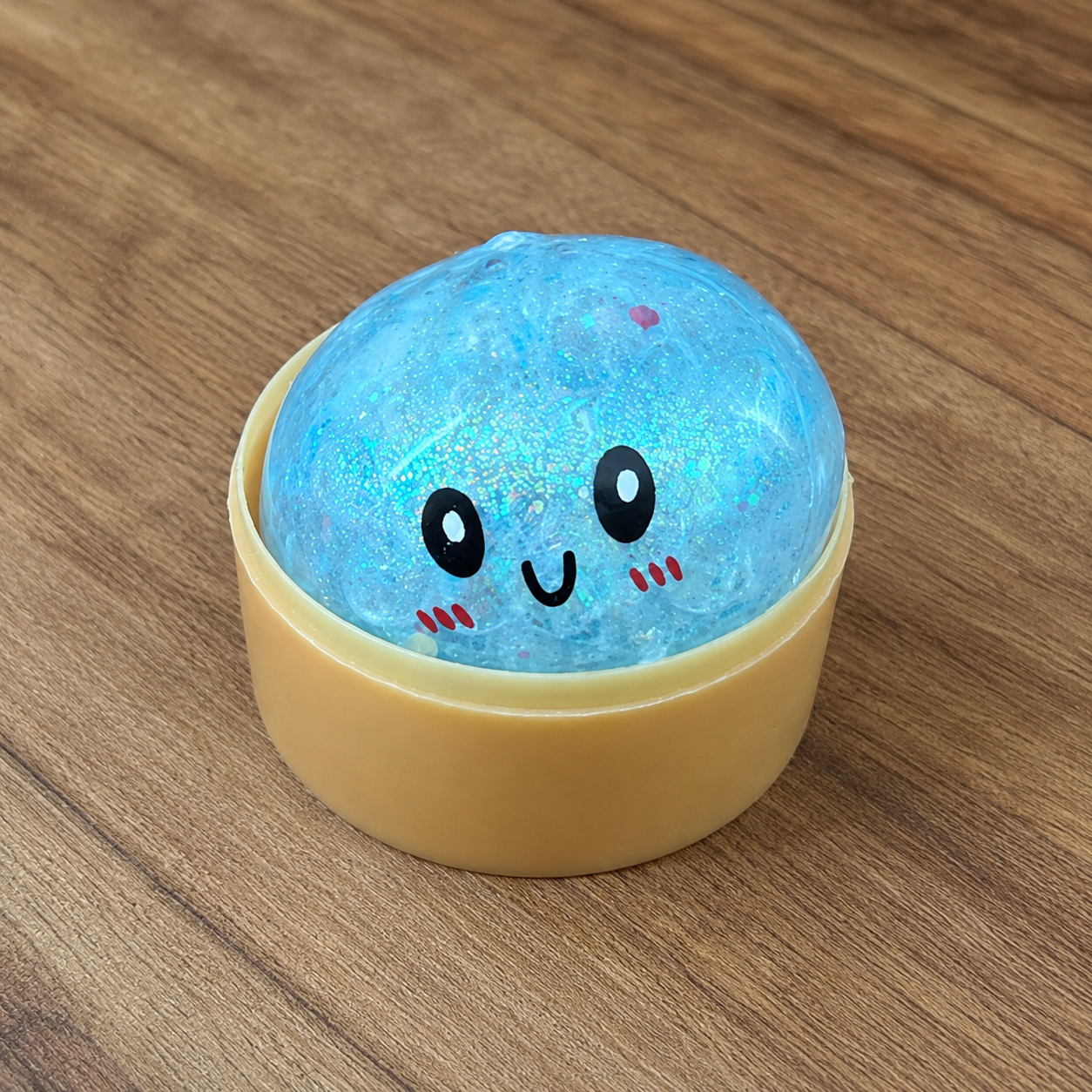a blue mystery bead-filled mini dumpling squishy with assorted colors, iridescent shimmer, kawaii face, steamer-style container, and soft sensory texture