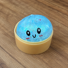 a blue mystery bead-filled mini dumpling squishy with assorted colors, iridescent shimmer, kawaii face, steamer-style container, and soft sensory texture
