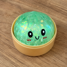 a green mystery bead-filled mini dumpling squishy with assorted colors, iridescent shimmer, kawaii face, steamer-style container, and soft sensory texture