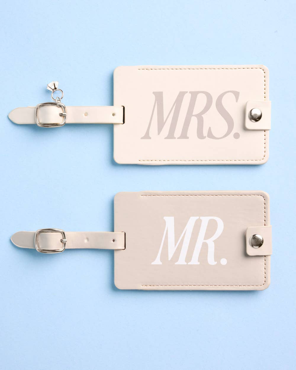Two beige luggage tags with 'MR.' and 'MRS.' text on a light blue background