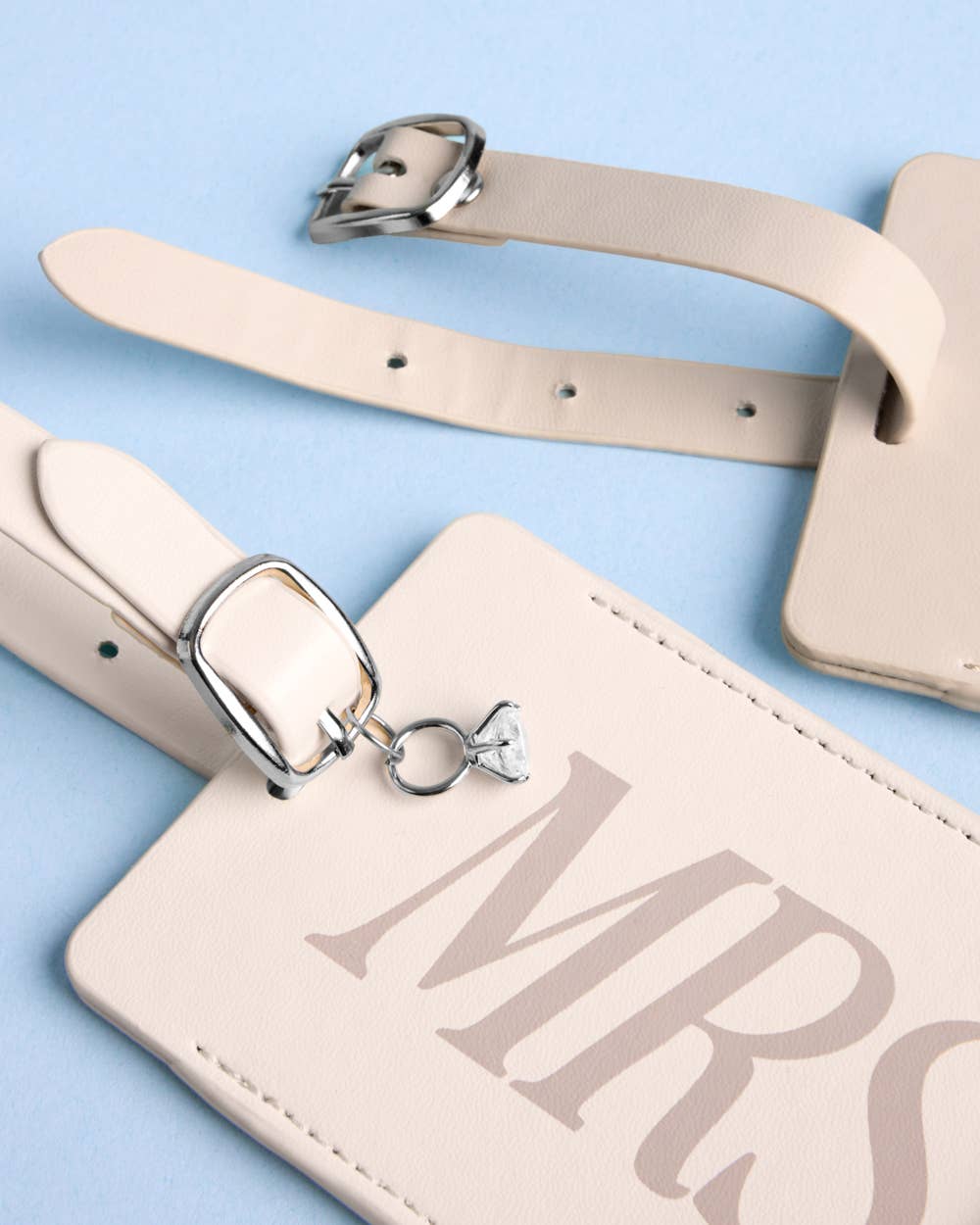 Beige luggage tag with 'MR' and decorative buckle on a light blue background