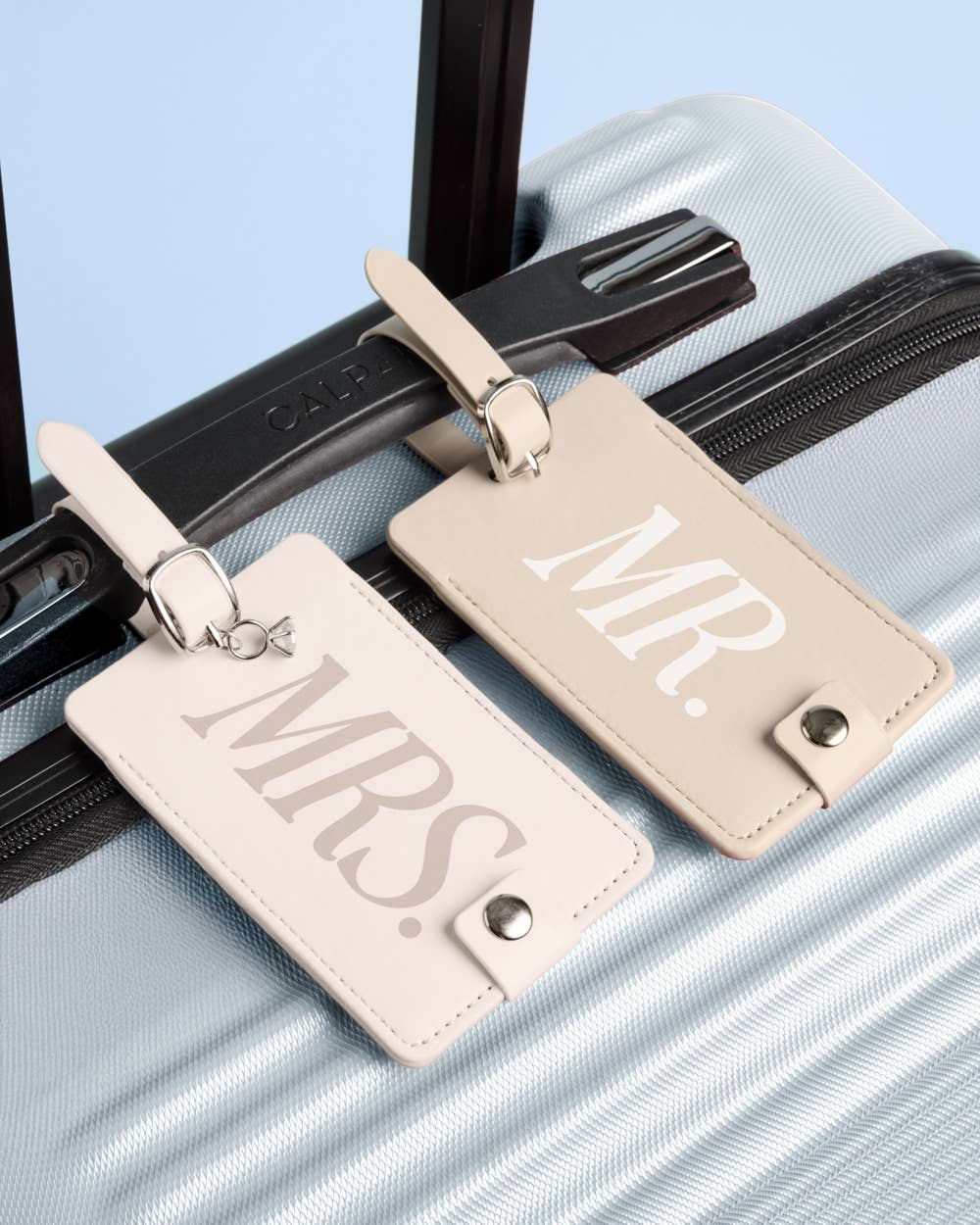 Two beige luggage tags labeled 'Mr.' and 'Mrs.' on a suitcase.