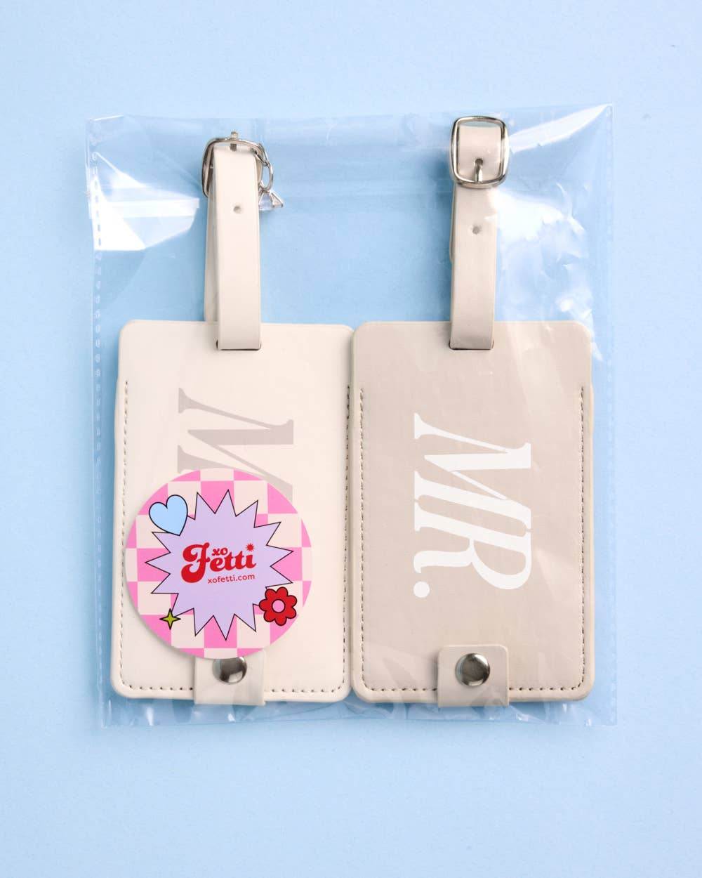 Two beige luggage tags with 'MR' and a colorful design on a light blue background