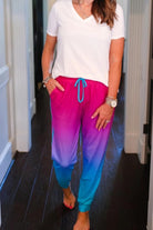 relaxed fit mid-rise joggers with side pockets and a tie waist drawstring, designed on a magenta to turquoise ombré print fabric with turquoise trim