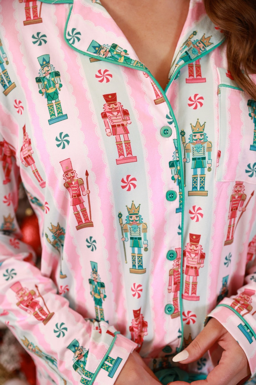a soft two-piece pajama set (long sleeves and pants) with alternating nutcracker, peppermint, and aqua-and-pink stripe patterns, sweet ruffle hem detail, coordinating aqua trim accents, a decorative aqua faux belt, and a comfy elastic waistband for an easy, relaxed fit