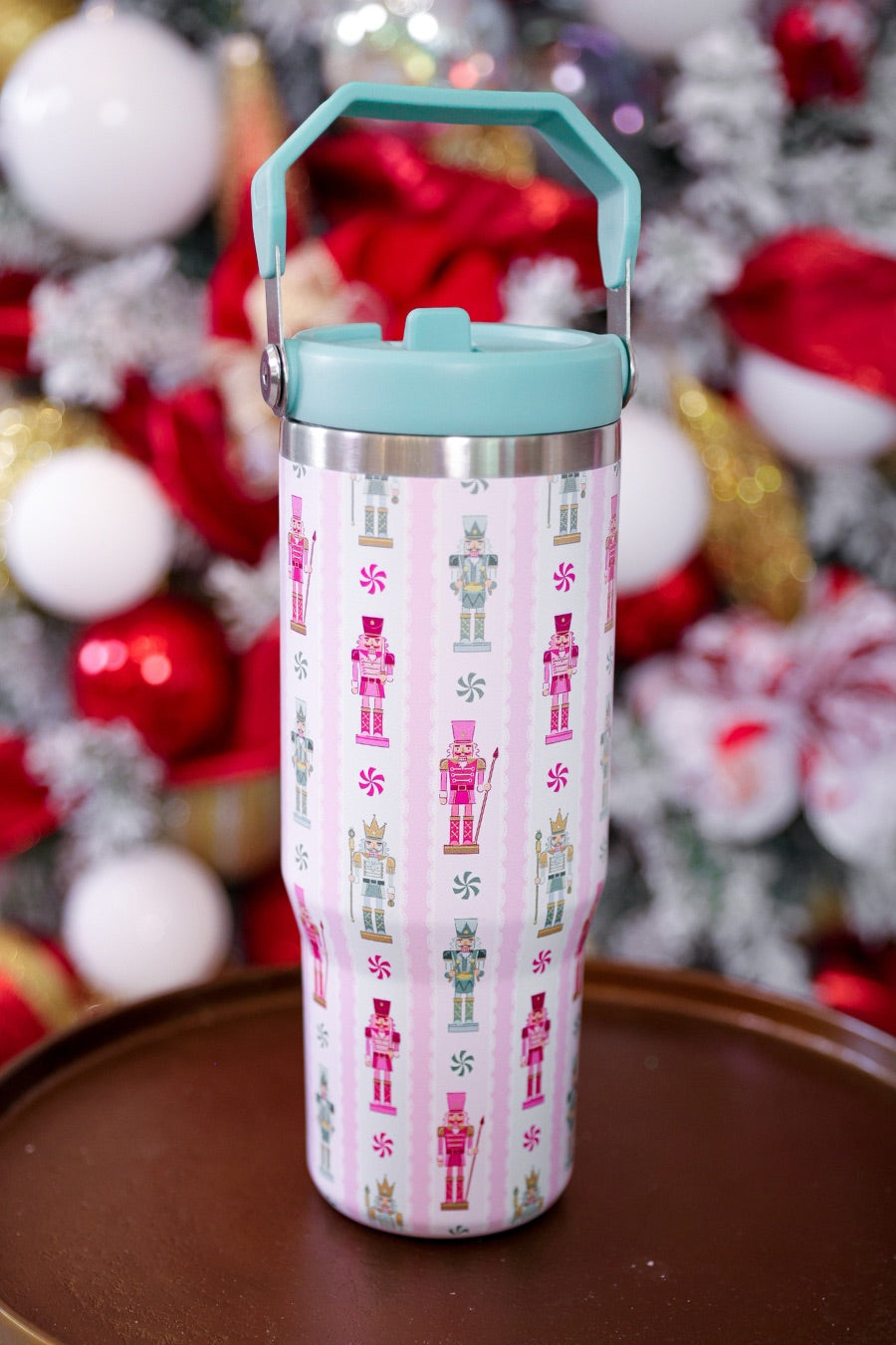 30-ounce striped pale pink insulated tumbler with a variety of whimsical multicolor pastel nutcrackers and peppermint swirls on white lace with a mint sturdy built-in handle, lid, and straw complete with silver hardware