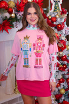 an oversized soft pink tee with sparkling multicolor sequin-embroidered nutcrackers, a contrasting aqua collar, and a relaxed fit