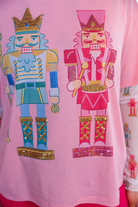 an oversized soft pink tee with sparkling multicolor sequin-embroidered nutcrackers, a contrasting aqua collar, and a relaxed fit