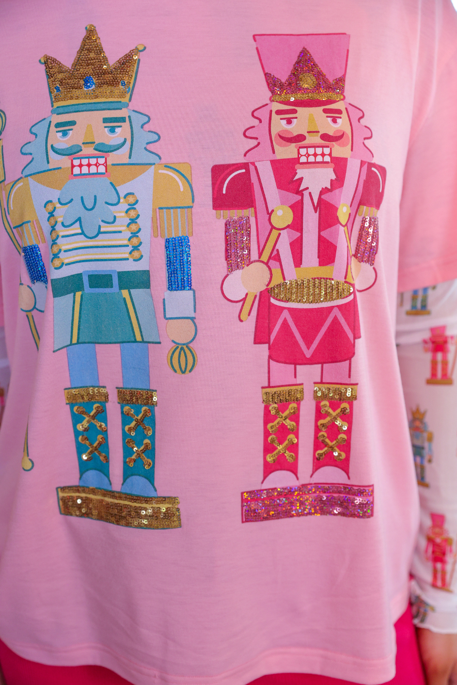 an oversized soft pink tee with sparkling multicolor sequin-embroidered nutcrackers, a contrasting aqua collar, and a relaxed fit