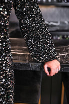 a black long balloon sleeve dress made of sparkly allover sequins, luxe velvet underlay, a keyhole accented upper back with button closure, a round neckline, and subtle elastic cuffs