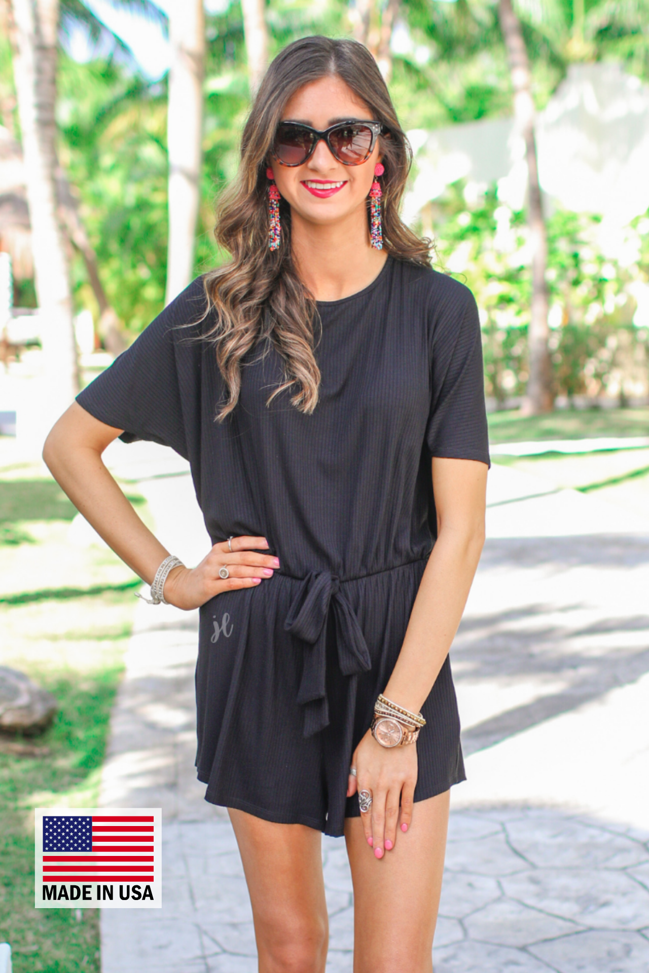 a black short-sleeve ribbed romper with a scoop neckline, a cutout tie back, an elastic waist with a faux tie detail, no pockets, and a relaxed, lightweight fit, accented with a MADE IN USA watermark in bottom left-hand corner