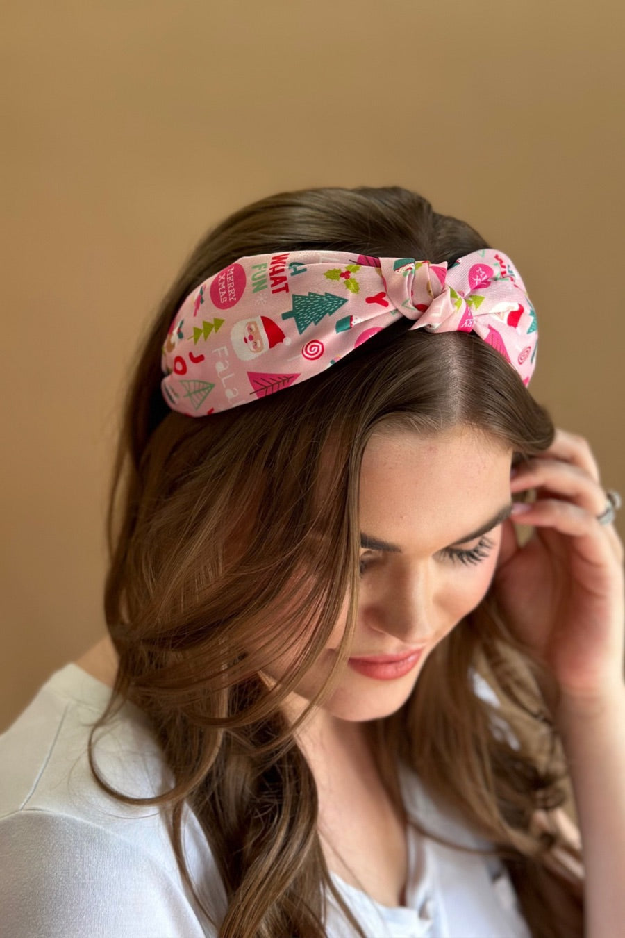 a twisted center top knot headband crafted from soft, lightweight pink fabric with a mix of holiday elements (cupcakes, lollipops, mistletoe, Santa, and trees) and joyful holiday sayings (Fa La La, Joy, Merry Xmas, and Oh What Fun)