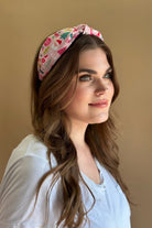 a twisted center top knot headband crafted from soft, lightweight pink fabric with a mix of holiday elements (cupcakes, lollipops, mistletoe, Santa, and trees) and joyful holiday sayings (Fa La La, Joy, Merry Xmas, and Oh What Fun)