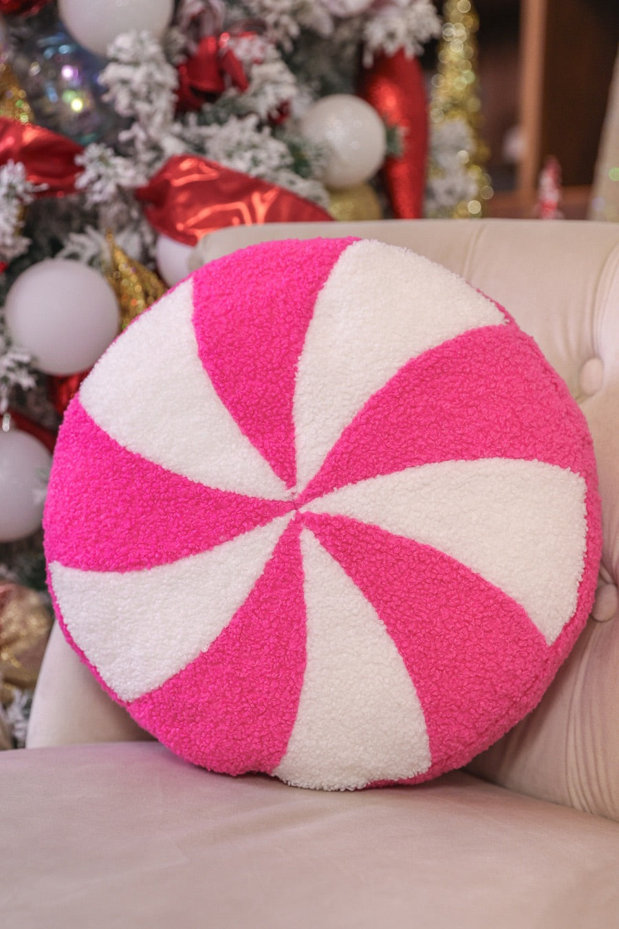 a round cushion with a bold hot pink and white peppermint swirl design on a soft, textured bouclé fabric
