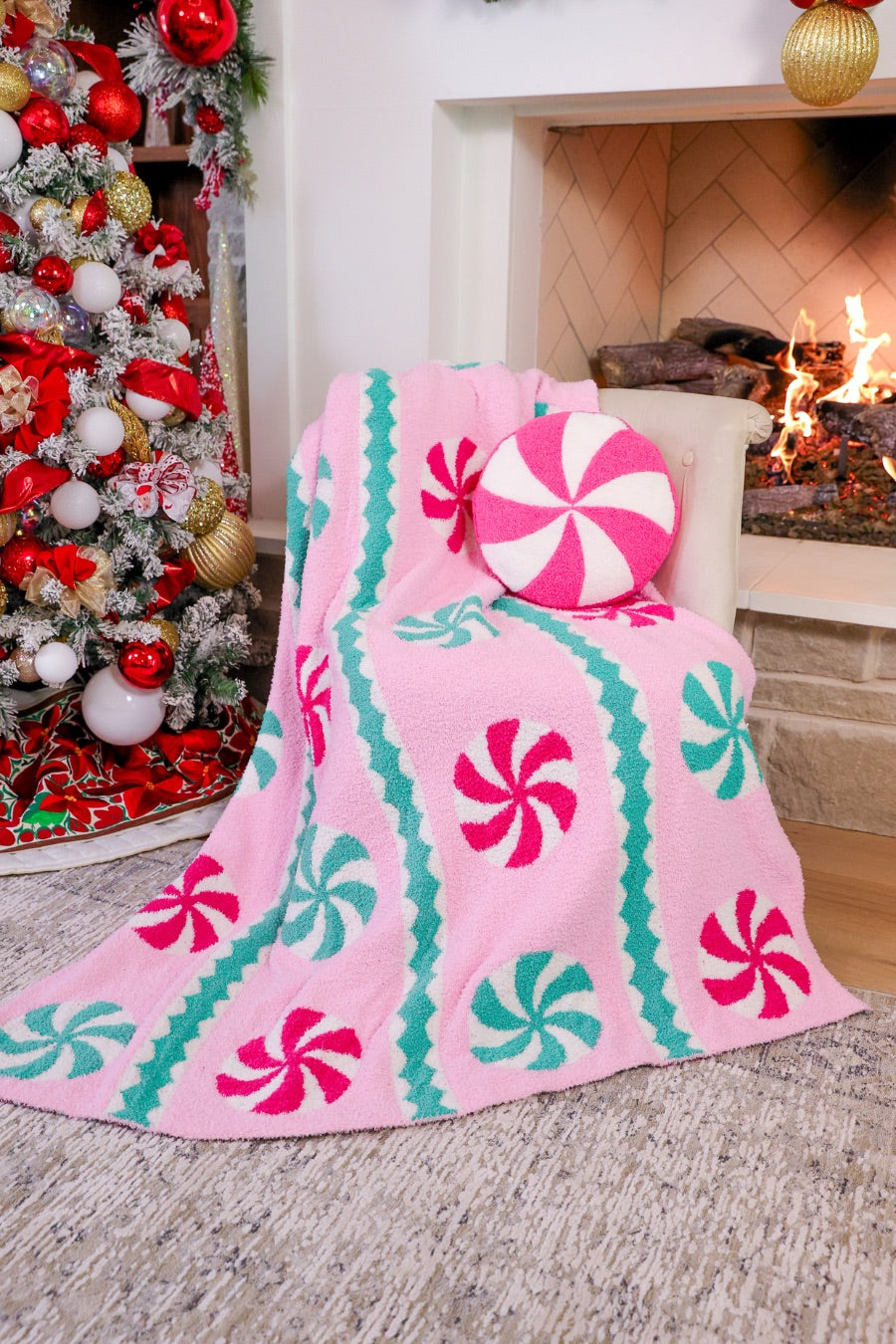 a round cushion with a bold hot pink and white peppermint swirl design on a soft, textured bouclé fabric paired with our Pink Wintermint Blanket