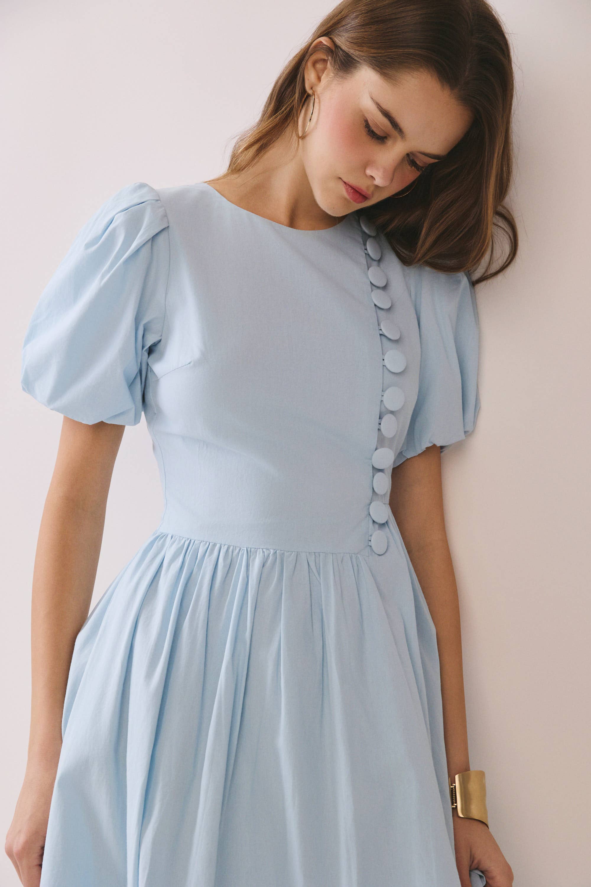 a baby blue puff sleeve midi dress with a rounded neckline, fitted bodice accented with fabric-covered faux buttons, gathered waist, full A-line skirt, side pockets, and a concealed back zipper