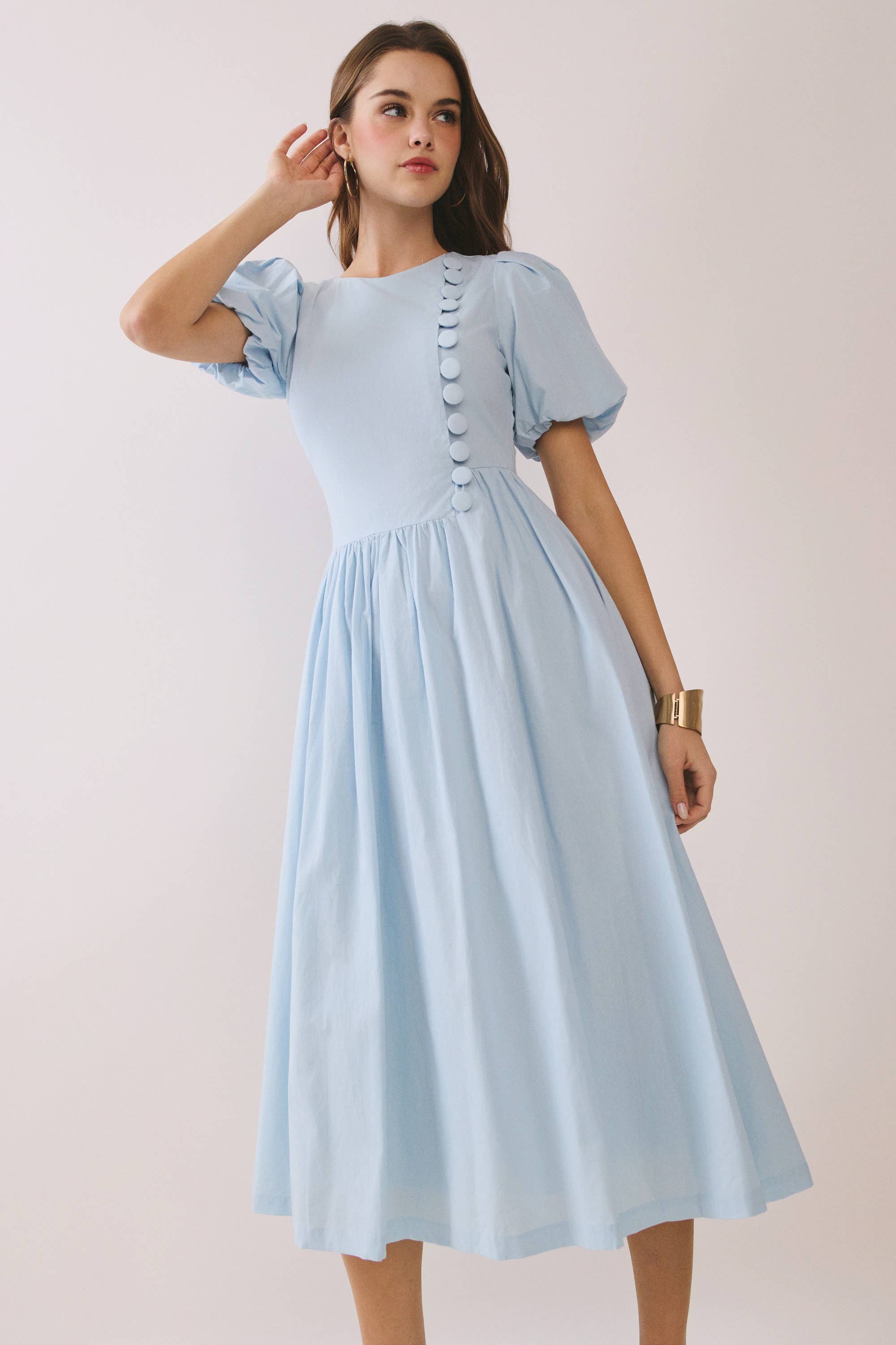 a baby blue puff sleeve midi dress with a rounded neckline, fitted bodice accented with fabric-covered faux buttons, gathered waist, full A-line skirt, side pockets, and a concealed back zipper