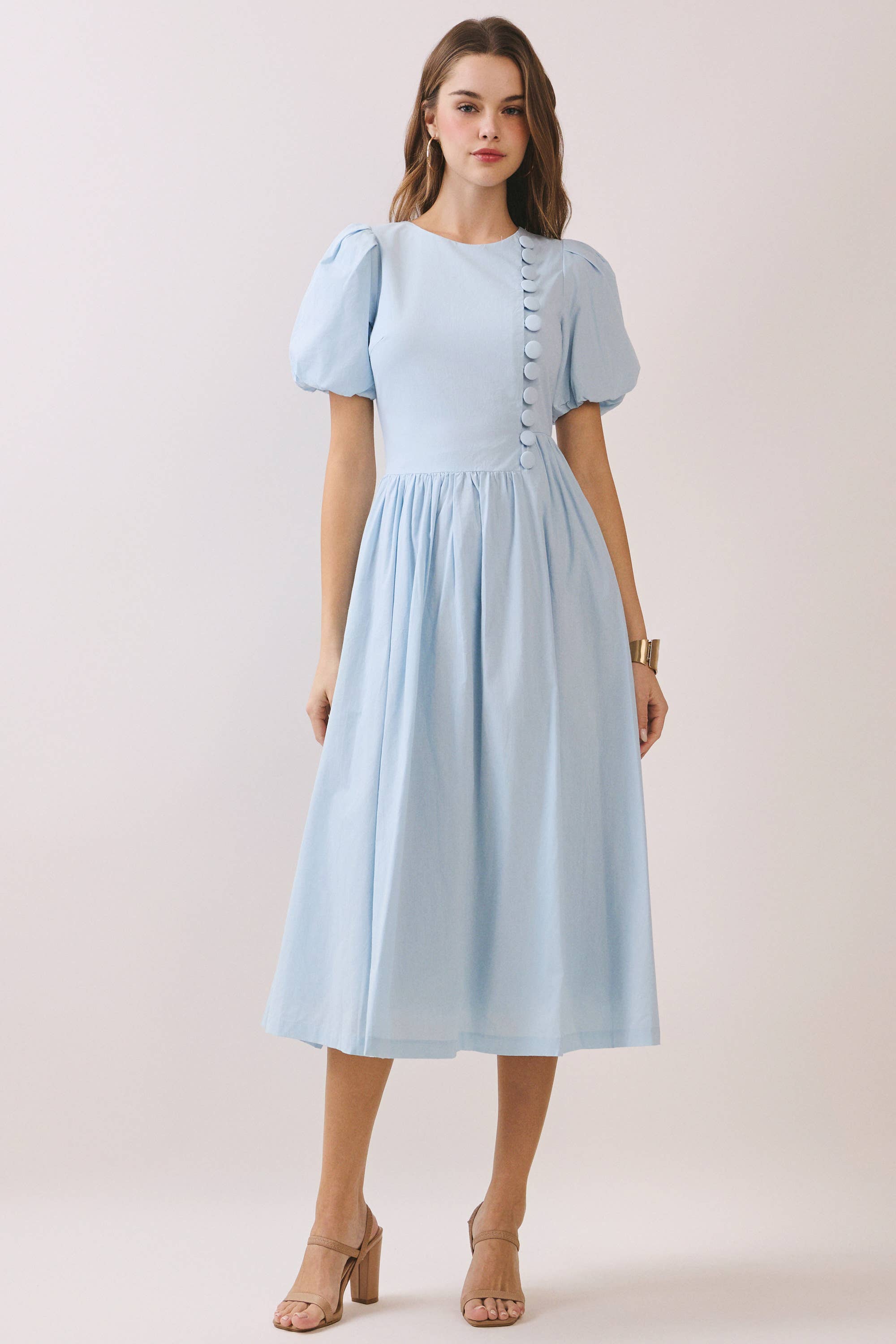 a baby blue puff sleeve midi dress with a rounded neckline, fitted bodice accented with fabric-covered faux buttons, gathered waist, full A-line skirt, side pockets, and a concealed back zipper