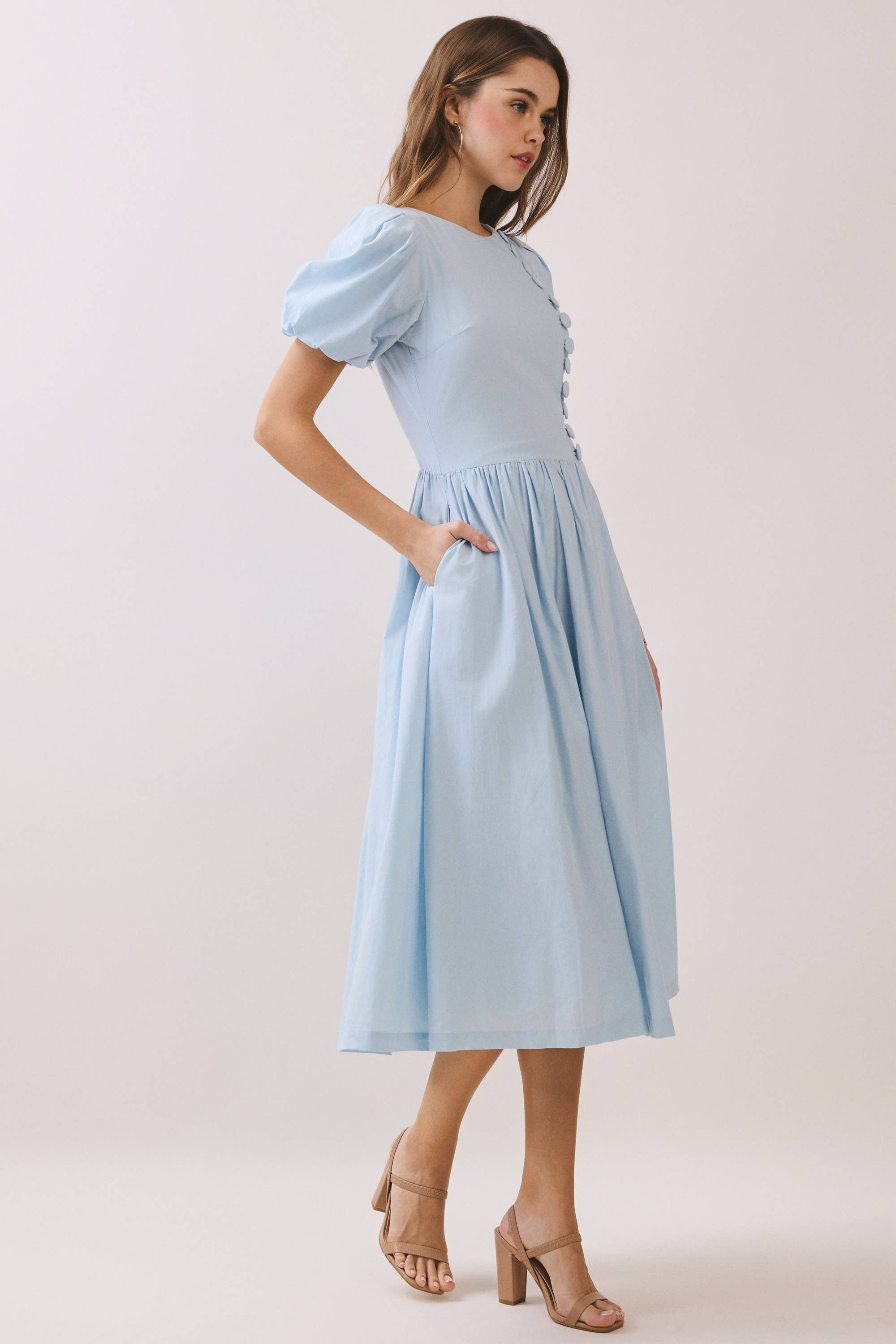 a baby blue puff sleeve midi dress with a rounded neckline, fitted bodice accented with fabric-covered faux buttons, gathered waist, full A-line skirt, side pockets, and a concealed back zipper
