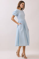 a baby blue puff sleeve midi dress with a rounded neckline, fitted bodice accented with fabric-covered faux buttons, gathered waist, full A-line skirt, side pockets, and a concealed back zipper