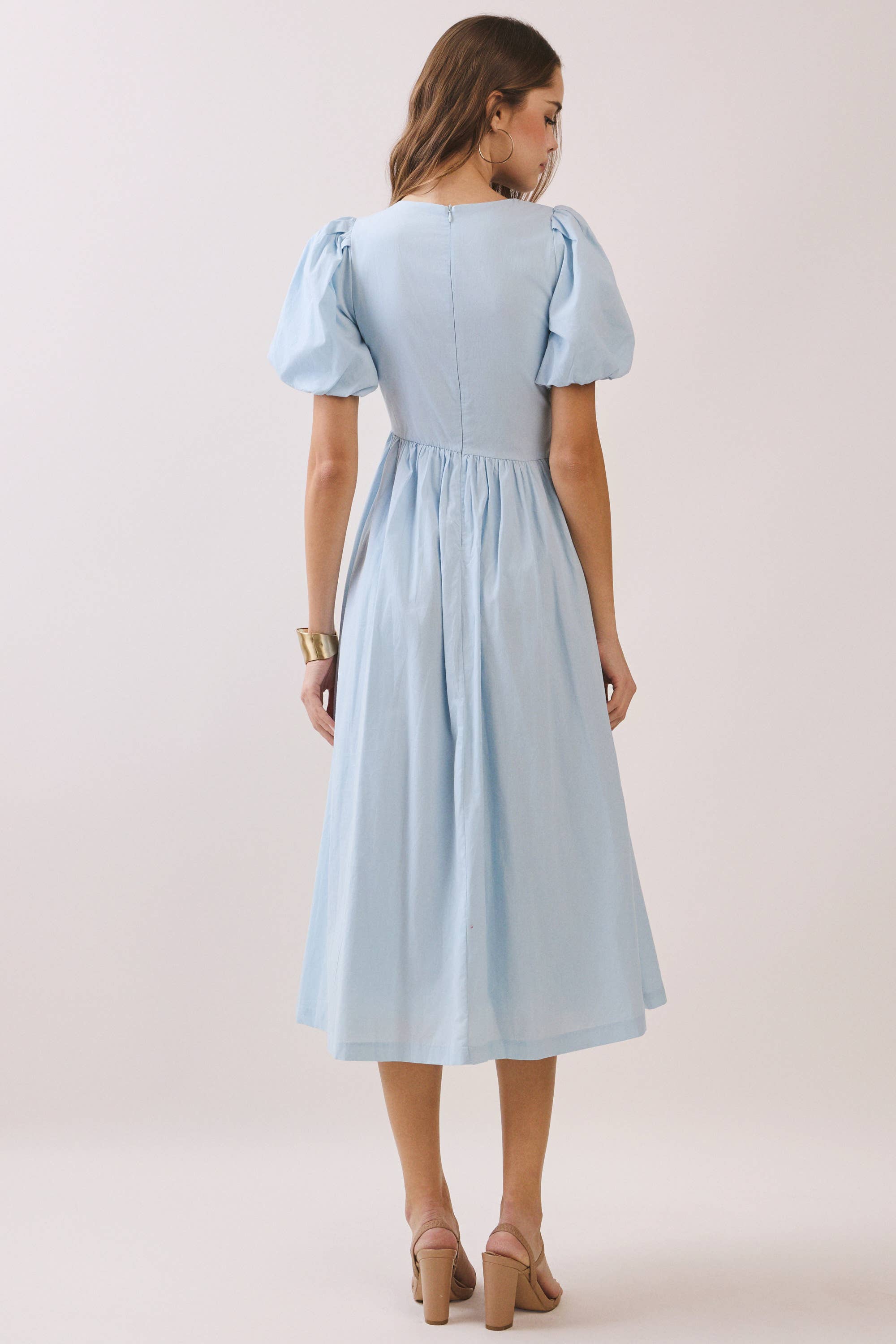 a baby blue puff sleeve midi dress with a rounded neckline, fitted bodice accented with fabric-covered faux buttons, gathered waist, full A-line skirt, side pockets, and a concealed back zipper