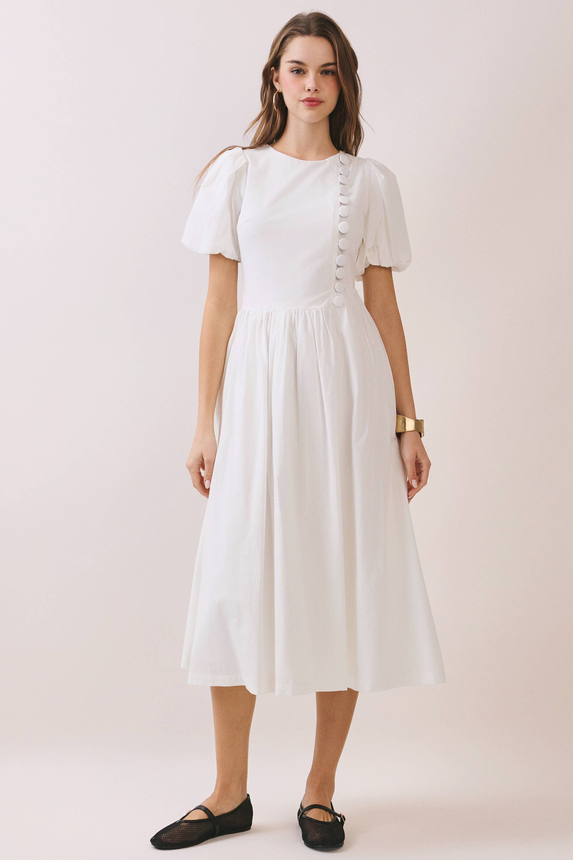 a white puff sleeve midi dress with a rounded neckline, fitted bodice accented with fabric-covered faux buttons, gathered waist, full A-line skirt, side pockets, and a concealed back zipper