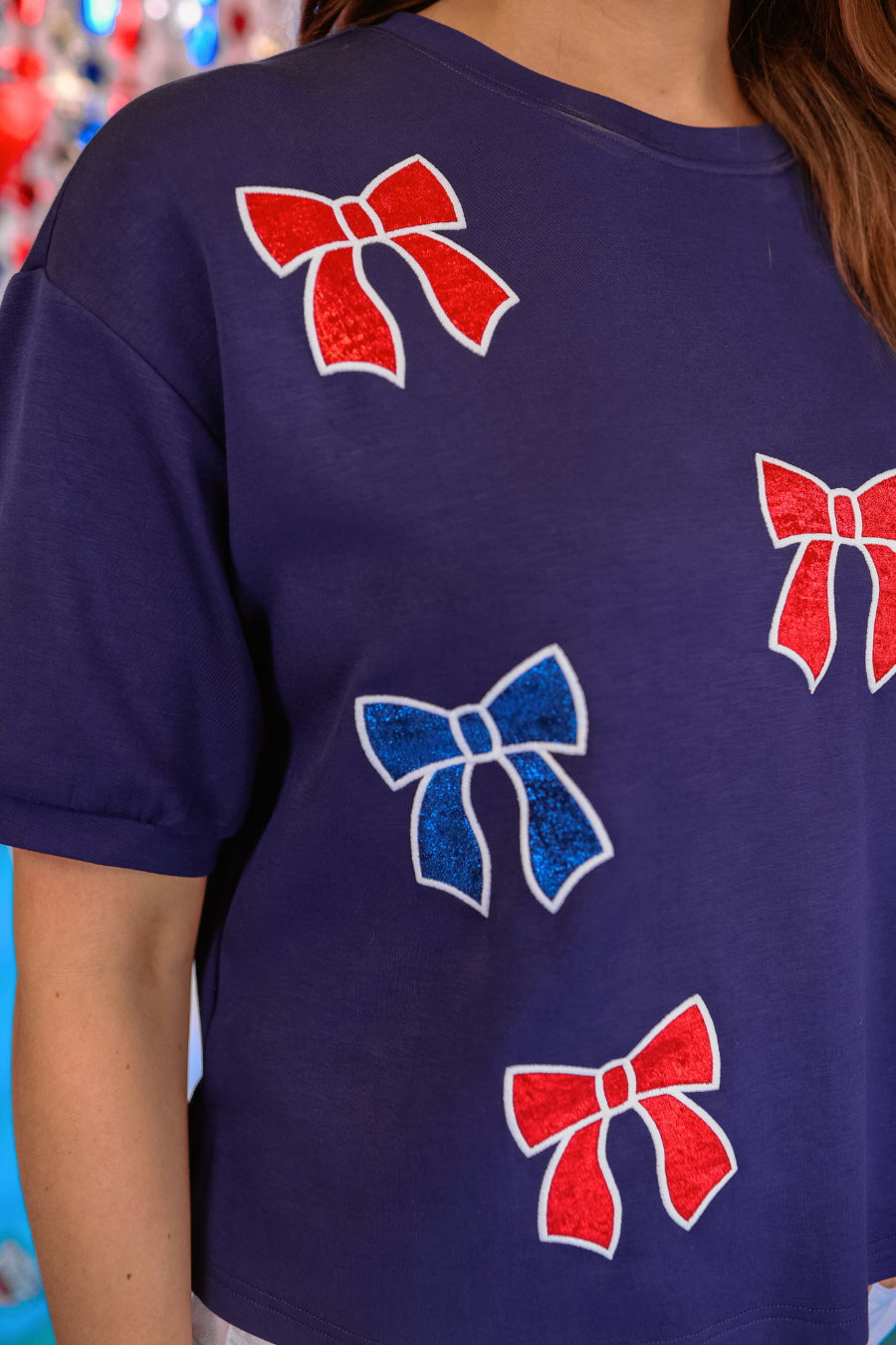 banded short-sleeved cropped fit luxe top with blue and red metallic foil bows outlined in white embroidery and side slits