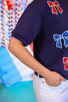 banded short-sleeved cropped fit luxe top with blue and red metallic foil bows outlined in white embroidery and side slits