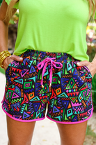 mid-rise relaxed fit activewear shorts with side pockets and a tie waist drawstring with gold bead accents, designed on a multicolor retro print fabric, black base, and fuchsia trim