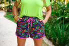 mid-rise relaxed fit activewear shorts with side pockets and a tie waist drawstring with gold bead accents, designed on a multicolor retro print fabric, black base, and fuchsia trim