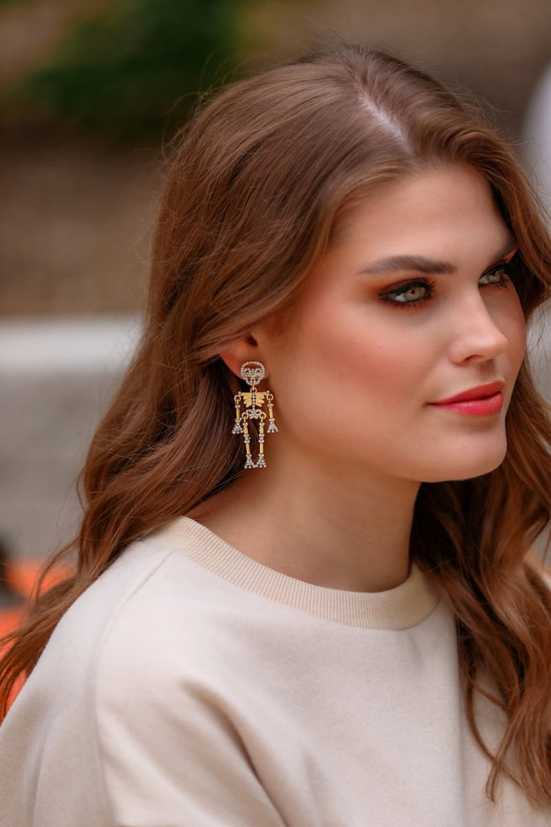 gold-plated post-back skeleton-shaped dangle earrings with rhinestone accents, skull stud tops, articulated bone design, matching barrel backs, and nickel/lead compliant construction in gold