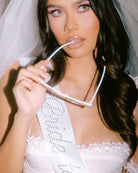 Woman in a white bridal outfit holding a clear visor.