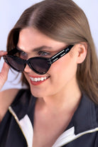 glossy black cat-eye sunglasses with dark lenses, silver and white raised accent on the temple, and brand name detail (on both the temple and the complimentary black pouch)