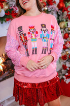 a lightweight pink long-sleeve top decorated with four vibrant nutcracker designs finished with dimensional beaded effect boots and accented by soft, shimmering velvet-sequin sleeves, a relaxed drop shoulder, and ribbed crew neckline, cuffs, and hem