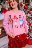 a lightweight pink long-sleeve top decorated with four vibrant nutcracker designs finished with dimensional beaded effect boots and accented by soft, shimmering velvet-sequin sleeves, a relaxed drop shoulder, and ribbed crew neckline, cuffs, and hem